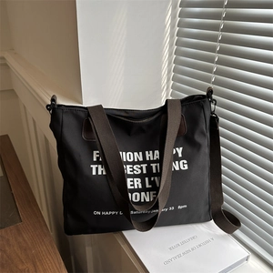 Black canvas tote bag with white lettering, brown straps, and adjustable shoulder strap