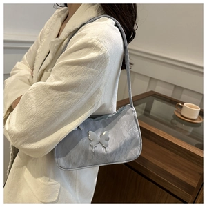 Gros plan du sac sous l'aisselle plissé bleu clair avec papillon argenté et texture métal