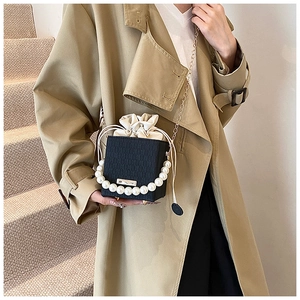 Detail of black bucket bag with pearl handle and golden chain on beige trench coat