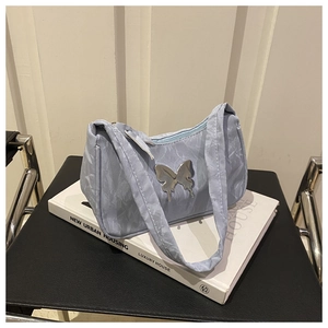 Détail du sac plissé bleu clair avec papillon argenté posé sur un livre blanc