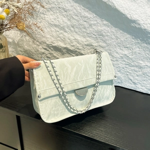 White faux leather crossbody bag with silver chain strap on black wooden surface