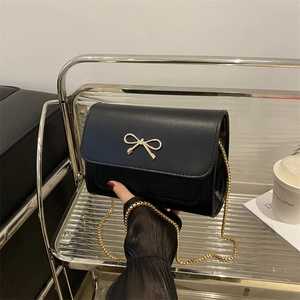 Luxurious black crossbody bag with gold bow clasp and elegant chain strap in a lifestyle shot