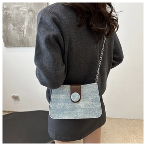 Detail of blue denim shoulder bag with brown leather flap and silver chain on model