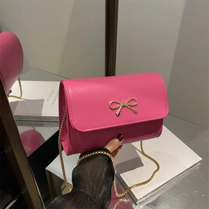 Chic magenta chain crossbody bag with golden bow clasp shown from a stylish hand-held angle