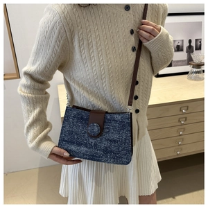 Détail du sac bandoulière en denim bleu avec rabat en cuir marron sur pull crème