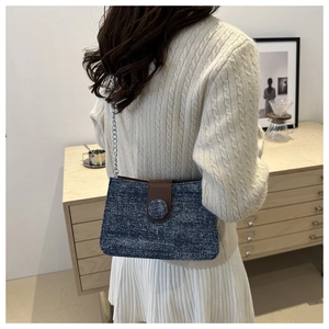 Detail of blue denim shoulder bag with brown leather flap and silver chain on model