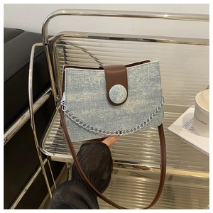 Détail d'un sac à bandoulière en denim bleu avec sangle en cuir marron et chaîne