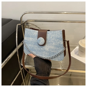 Détail du sac bandoulière en jean bleu avec garniture en cuir brun et chaîne argent