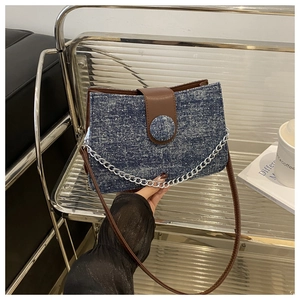 Détail du sac bandoulière en denim bleu avec rabat en cuir marron et chaîne argentée