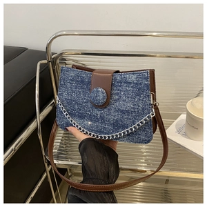 Détail d'un sac à bandoulière en denim bleu avec garniture en cuir brun et chaîne argent