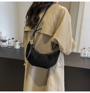 Detail of black suede crescent bag with knotted shoulder strap and gold zipper closure