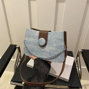 Blue denim and brown leather shoulder bag with chain strap on a designer chair