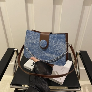 Blue denim crossbody bag with brown leather trim and silver chain strap on black chair