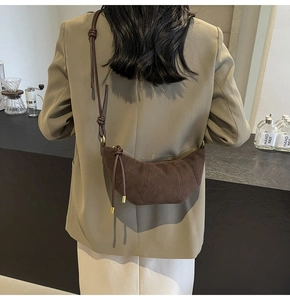 Detail of dark brown suede crescent bag featuring knotted strap and metal hardware accents