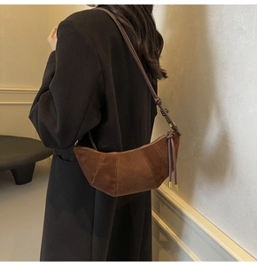 Detail of a brown suede croissant bag with curved stitching and knotted shoulder strap