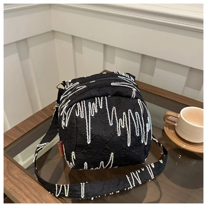 Détail du sac coquillage noir avec broderie ondulée sur une table de café