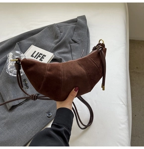 Detail of a brown suede croissant bag with stitching and fine cord shoulder strap