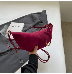 Detail of burgundy suede croissant bag with pleated design and knotted rope strap accents