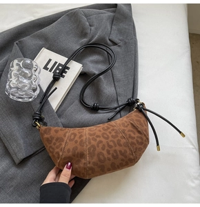 Detail of a croissant-shaped leopard print bag with suede texture and knotted leather strap