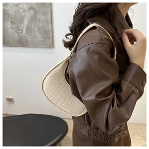 Detail of cream crocodile embossed crescent bag worn with a leather jacket