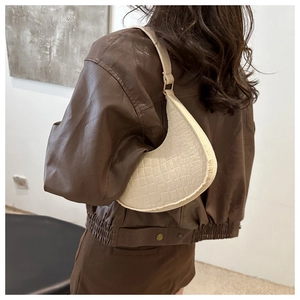Detailed view of cream crocodile-embossed half-moon bag worn by a model over the shoulder