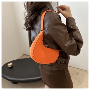 Model wearing a bright orange croc-effect crescent underarm bag with a brown leather jacket