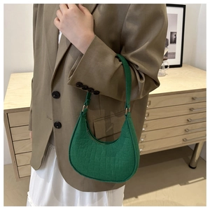 Detail of emerald green faux crocodile texture on a chic shoulder bag held by a model