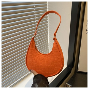 Close-up of bright orange crescent hobo bag with textured crocodile pattern and wide handle