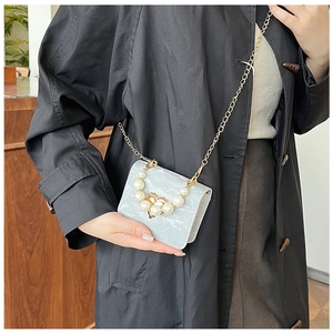 Detailed view of mini crossbody bag with pearl handle and golden heart buckle