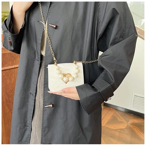 Detail of cream mini crossbody bag featuring pearl charm and gold heart hardware