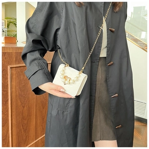 Detail of white mini handbag featuring pearl handle and gold chain strap on black coat