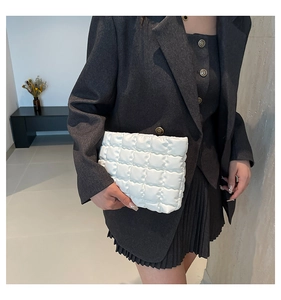 Gros plan sur la pochette matelassée blanche tenue par un mannequin en blazer gris