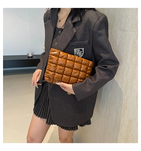 Détail d'une pochette nuage matelassée marron tenue par un mannequin en costume gris