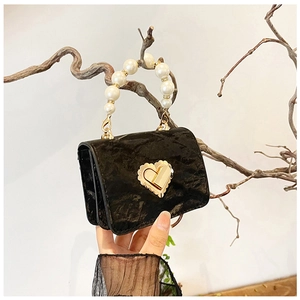 Detail of a mini black handbag featuring a pearl handle and golden heart twist-lock
