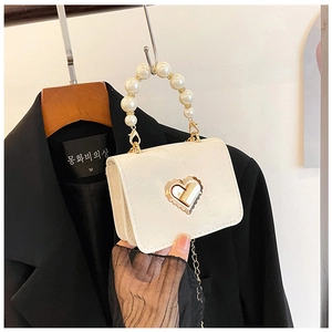 Detail of cream white patent leather mini bag with pearl handle and gold heart lock