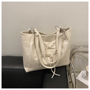 Close-up of cream tote bag featuring lace-up bow design and silver metal ring hardware