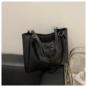 Detail of black leather tote bag with ribbon bow and silver metal eyelets on a sofa