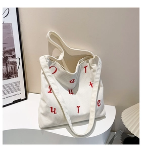 Détail du sac cabas en velours côtelé crème avec broderie de lettres rouges et texture