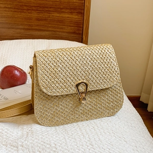 Chic beige straw woven crossbody bag with golden horseshoe clasp on a cozy bed
