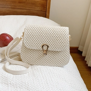 Fashionable cream woven crossbody bag with artistic gold lock shown on white bedding