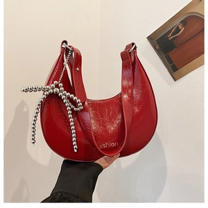 Detail of red crescent bag with glossy patent leather finish and silver bow charm