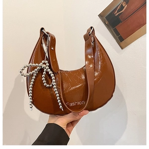 Detail of a brown patent leather crescent bag with a silver beaded bow and Fashion logo