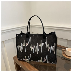 Détail du sac cabas noir avec broderie vagues colorées et texture jacquard sur table en bois