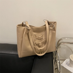 Minimalist beige tote bag with bow tie straps and silver ring hardware on a leather sofa