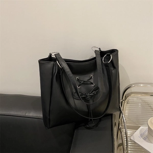 Minimalist black leather tote bag with bow tie design and silver ring on a leather sofa