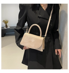 Dettaglio di una borsa a tracolla beige minimalista con trama scamosciata e fibbie metalliche