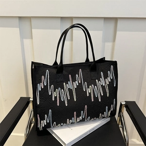 Grand sac cabas noir avec broderie zigzag colorée posé sur un fauteuil noir