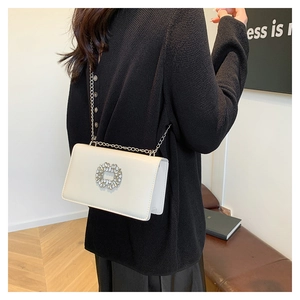Detailed view of square rhinestone buckle and golden chain on white crossbody bag