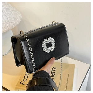 Detail of black glossy square bag featuring a large sparkling diamond buckle and chain