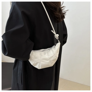 Close-up of white crescent crossbody bag with pleated texture and stylish knotted strap